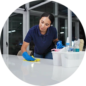 Unterhaltsreinigung im Büro – professionelle Reinigungskraft bei der Arbeit Professionelle Unterhaltsreinigung: Reinigungskraft säubert einen Tisch mit Reinigungsmitteln und Handschuhen in einem modernen Büro.