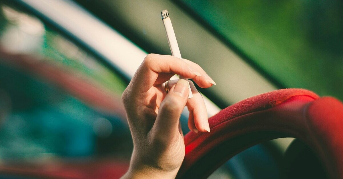 Hand mit Zigarette auf Lenkrad beim Rauchen im Auto