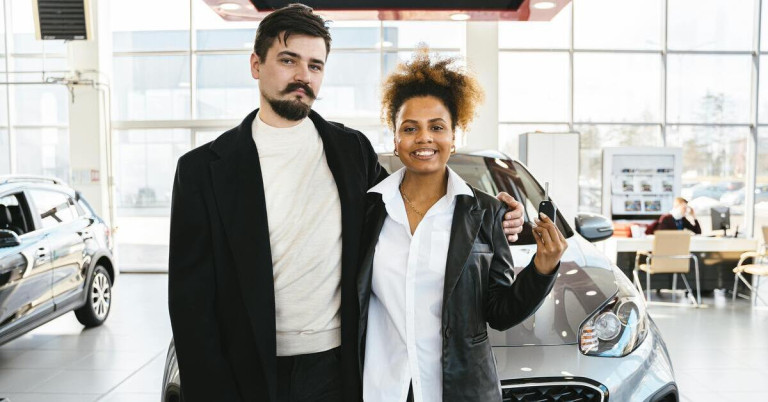 Paar steht vor neuem Auto im Autohaus und hält Autoschlüssel