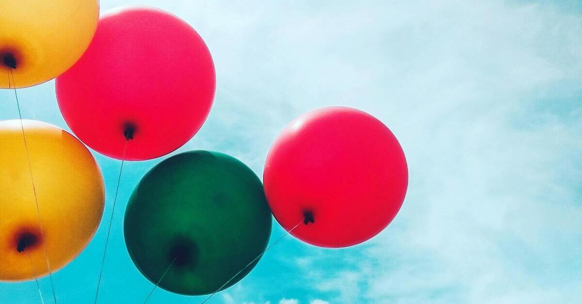 Drei bunte Luftballons vor blauem Himmel, zwei rote und ein grüner Ballon