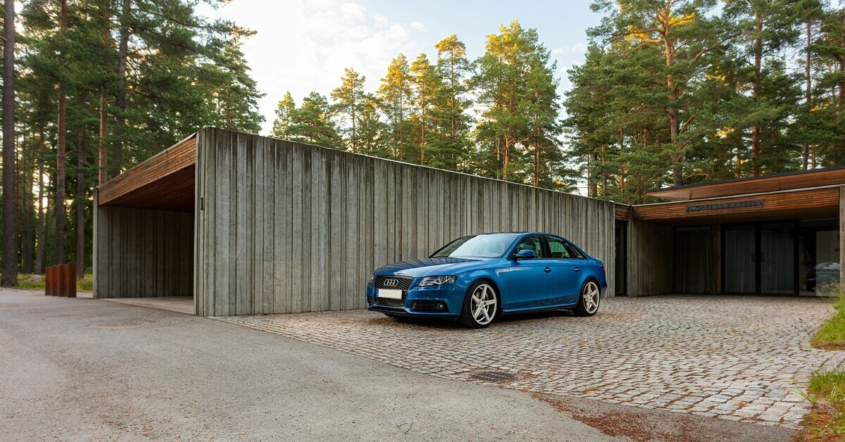 Blaues Auto neben Garage im Wald, moderner Audi auf Kopfsteinpflaster