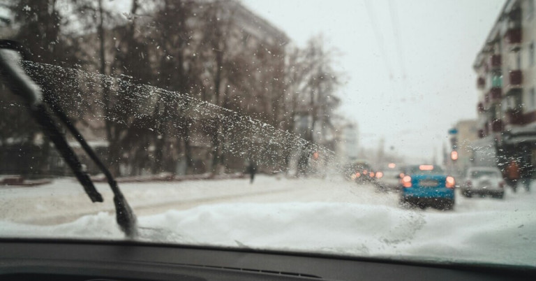 Vereiste Autoscheibe im Winter mit Blick auf verschneite Straße