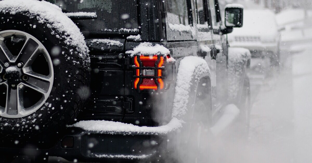 Jeep im Winter mit Schnee auf dem Fahrzeug und eingeschaltetem Rücklicht