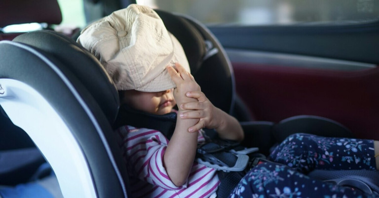 Mädchen im Kindersitz mit gestreiftem Shirt und heller Mütze im Auto