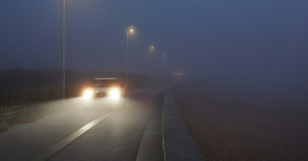 Auto mit eingeschaltetem Nebelscheinwerfer auf einer nebligen Straße bei Nacht