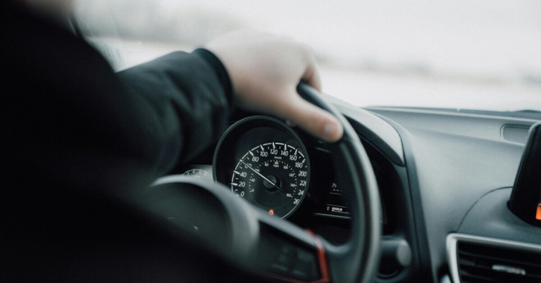 Autofahrer hält das Lenkrad und blickt auf den Tacho im Auto
