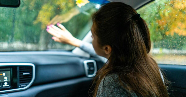 Frau wischt Kondenswasser von einer Autoscheibe im Innenraum eines Fahrzeugs