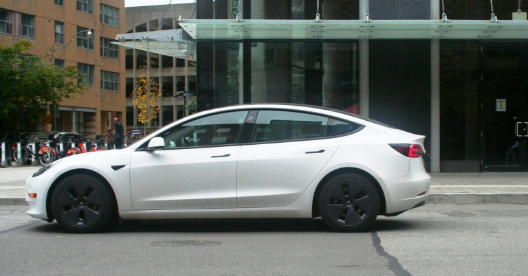 Weißes Elektroauto auf einer Straße vor einem modernen Gebäude