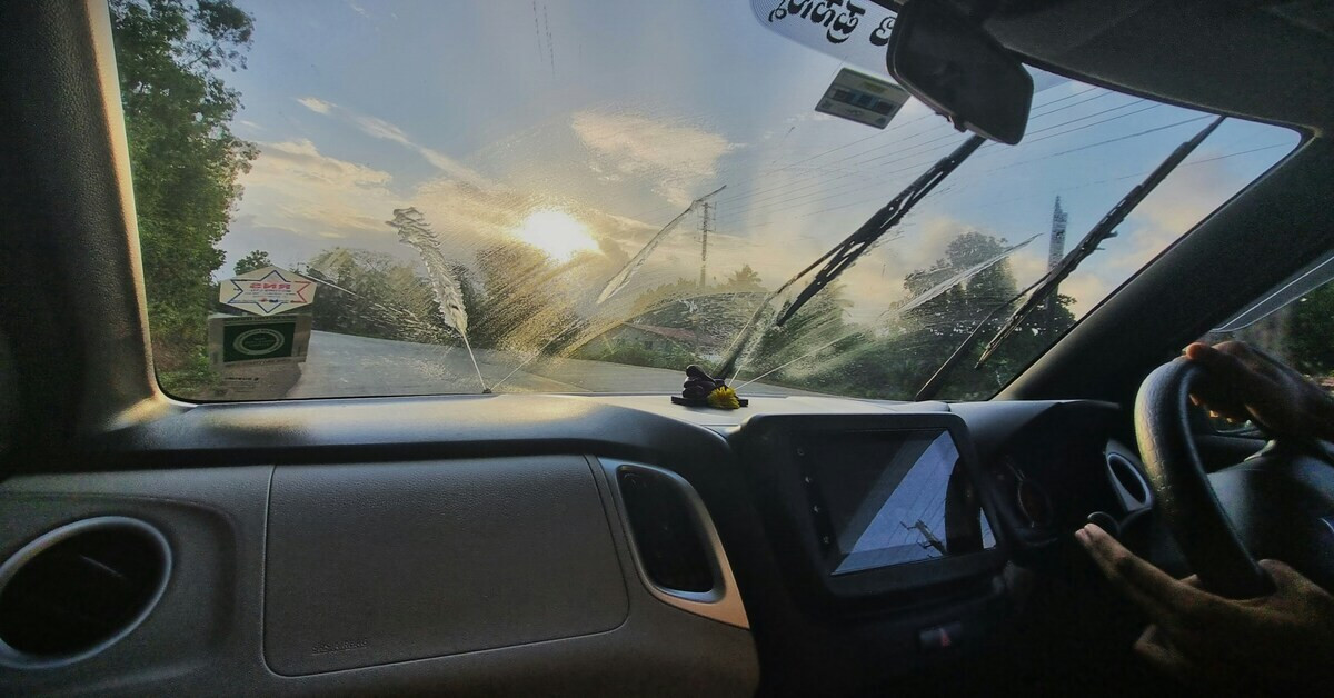 Blick aus einem Auto mit nasser Windschutzscheibe bei Sonnenaufgang, fotografiert von Nikhil auf Unsplash