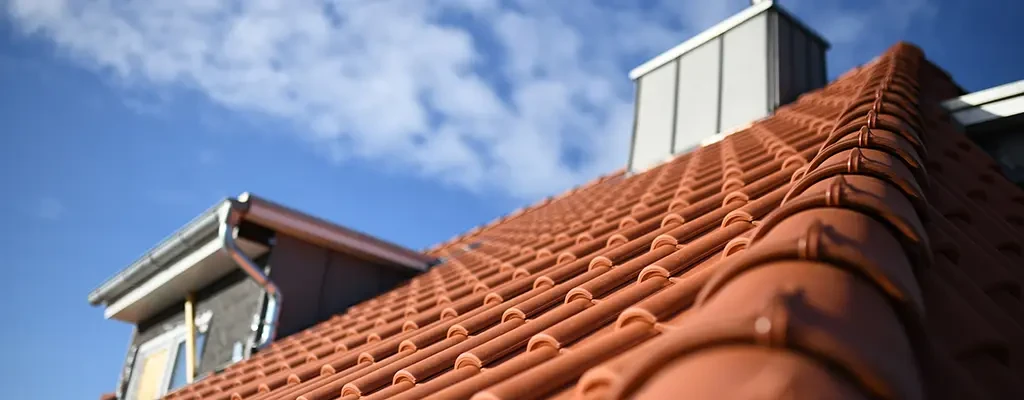 Dachdeckerarbeiten an einem Ziegeldach unter blauem Himmel