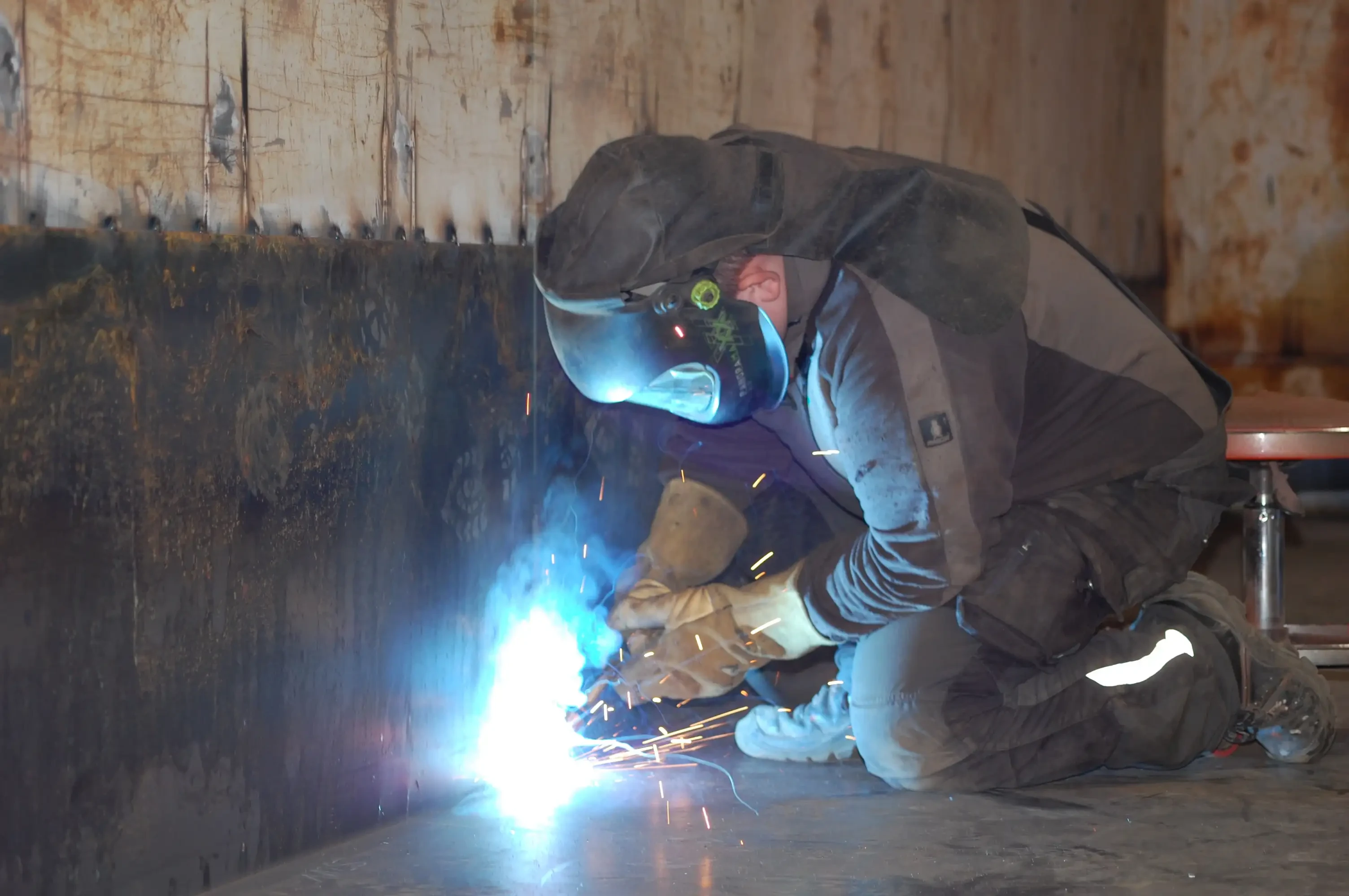 Schweißer bei der Arbeit mit Schutzhelm und Funkenflug in einer Werkstatt