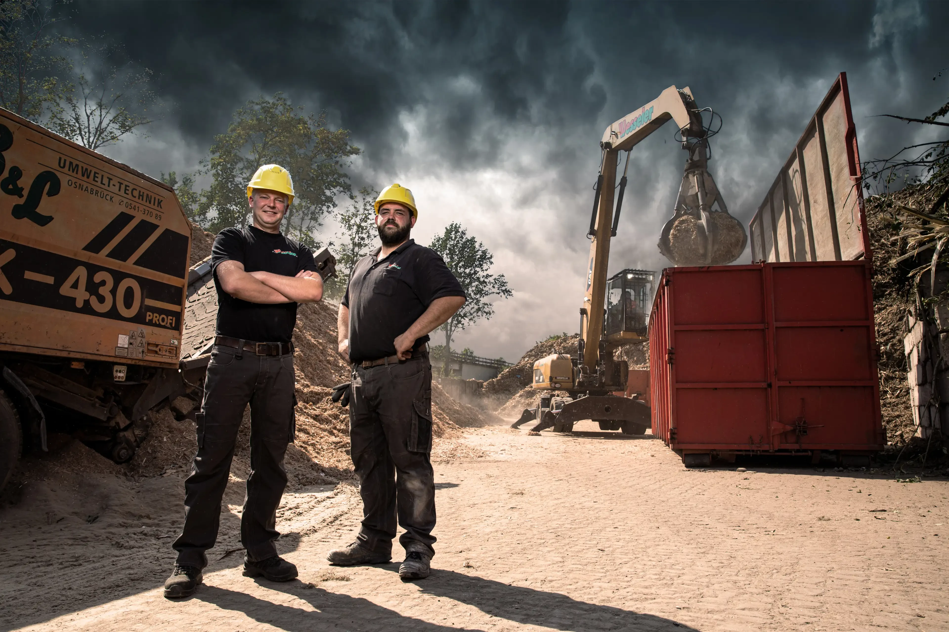 Zwei Bauarbeiter mit gelben Helmen auf einer Baustelle vor einem Bagger und Containern
