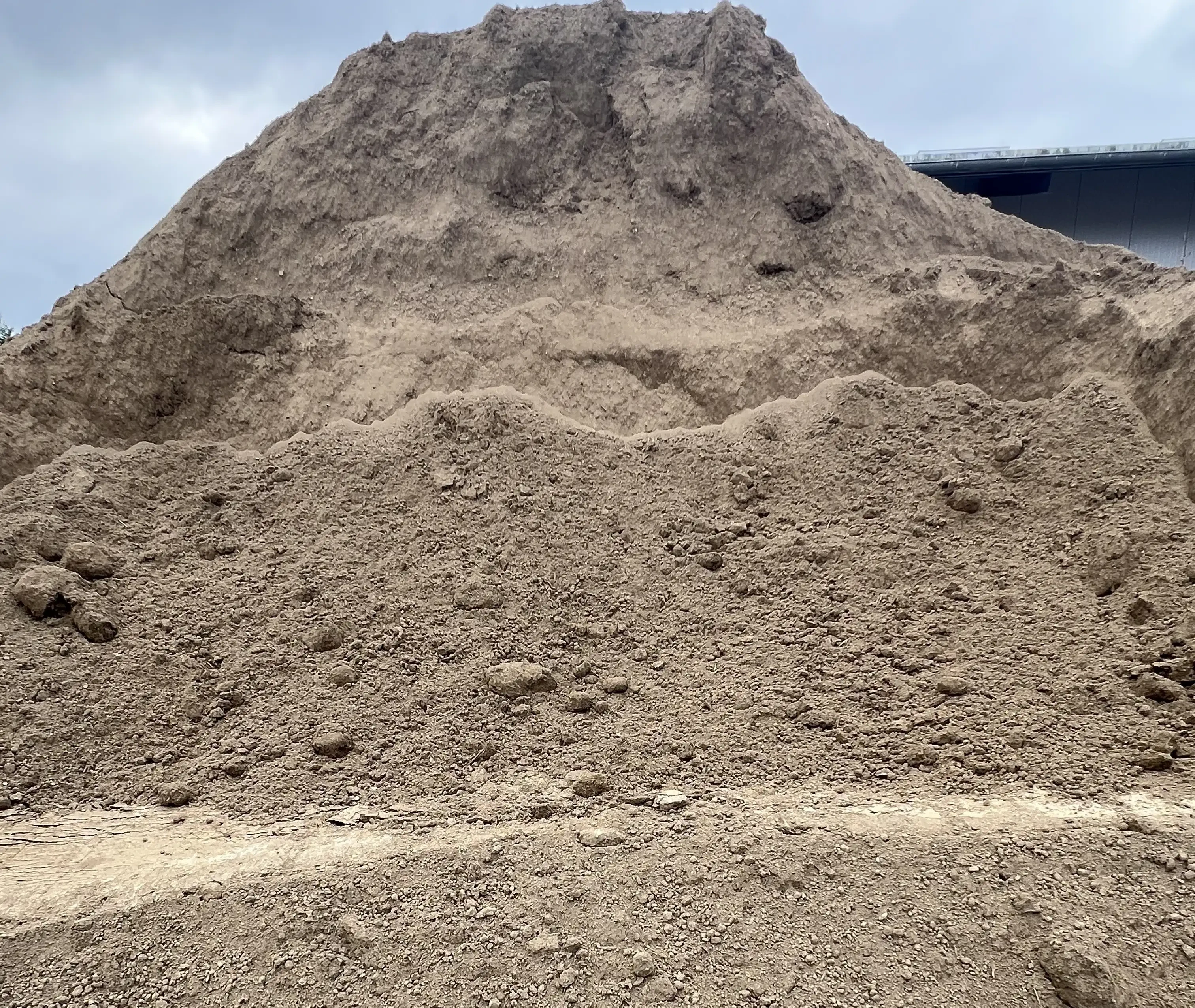 Großer Sand- oder Erdhügel auf einer Baustelle unter bewölktem Himmel