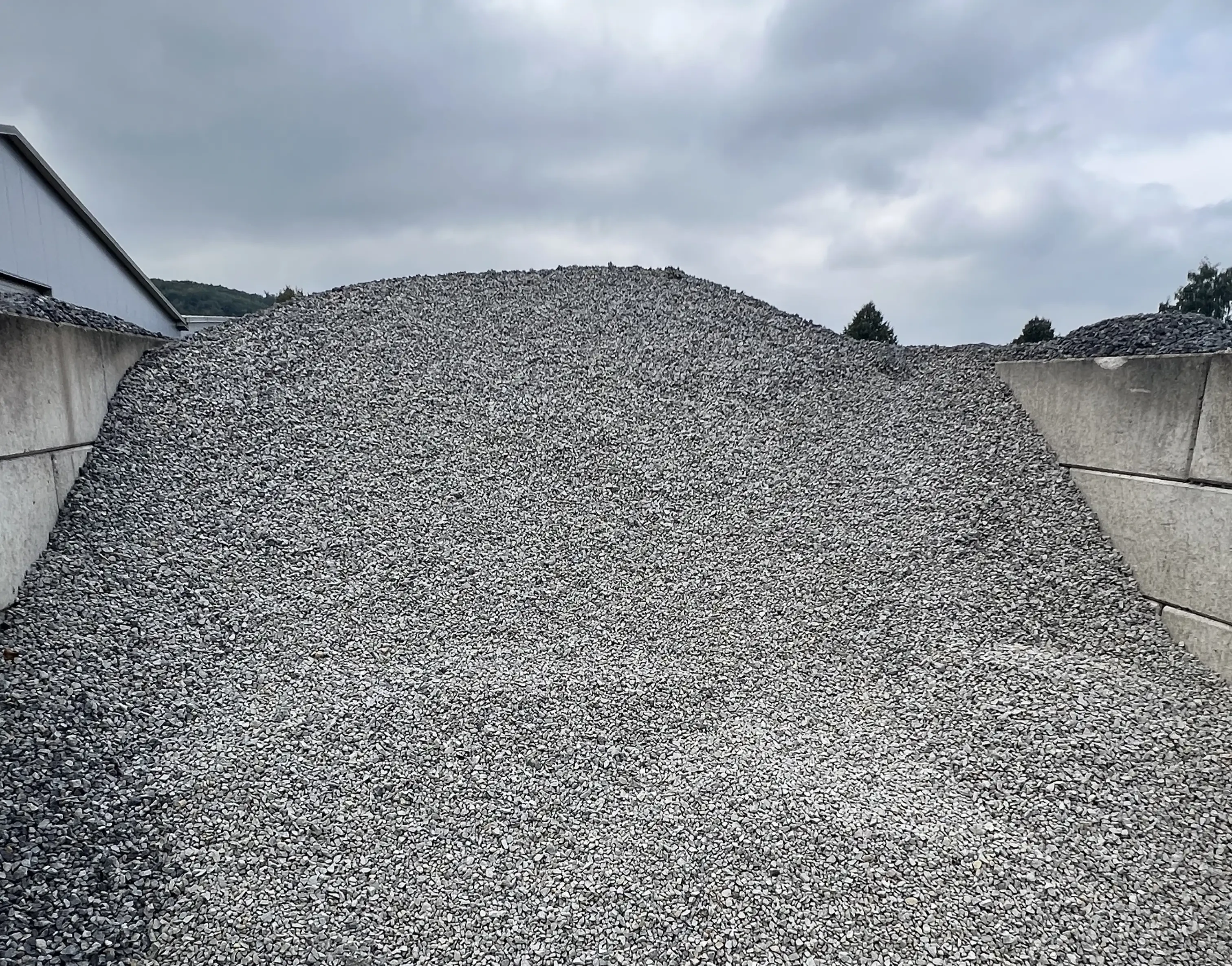 Großer Schotterhaufen auf einem Lagerplatz unter bewölktem Himmel
