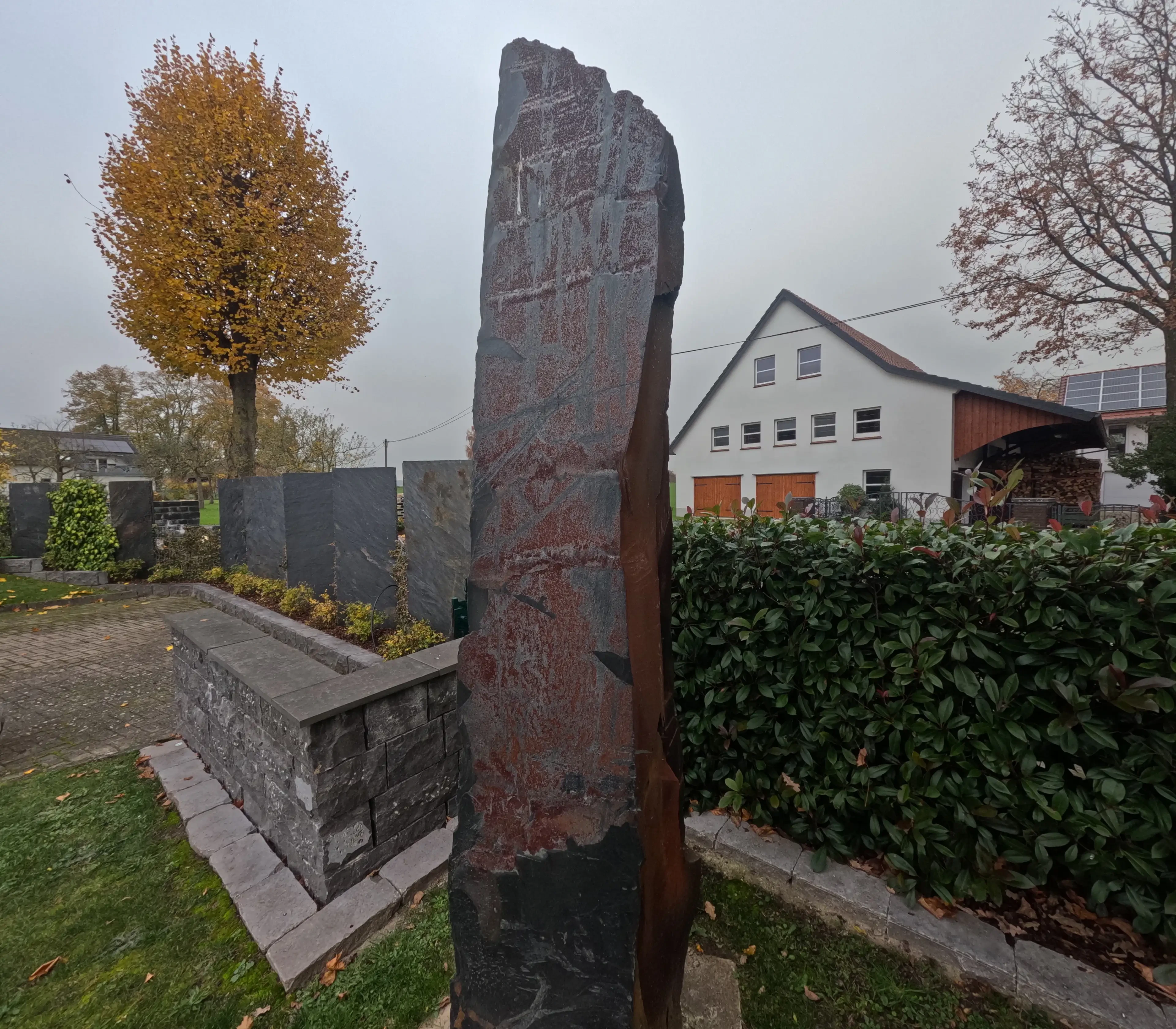 Monolith aus Naturstein im Garten vor einem modernen Haus