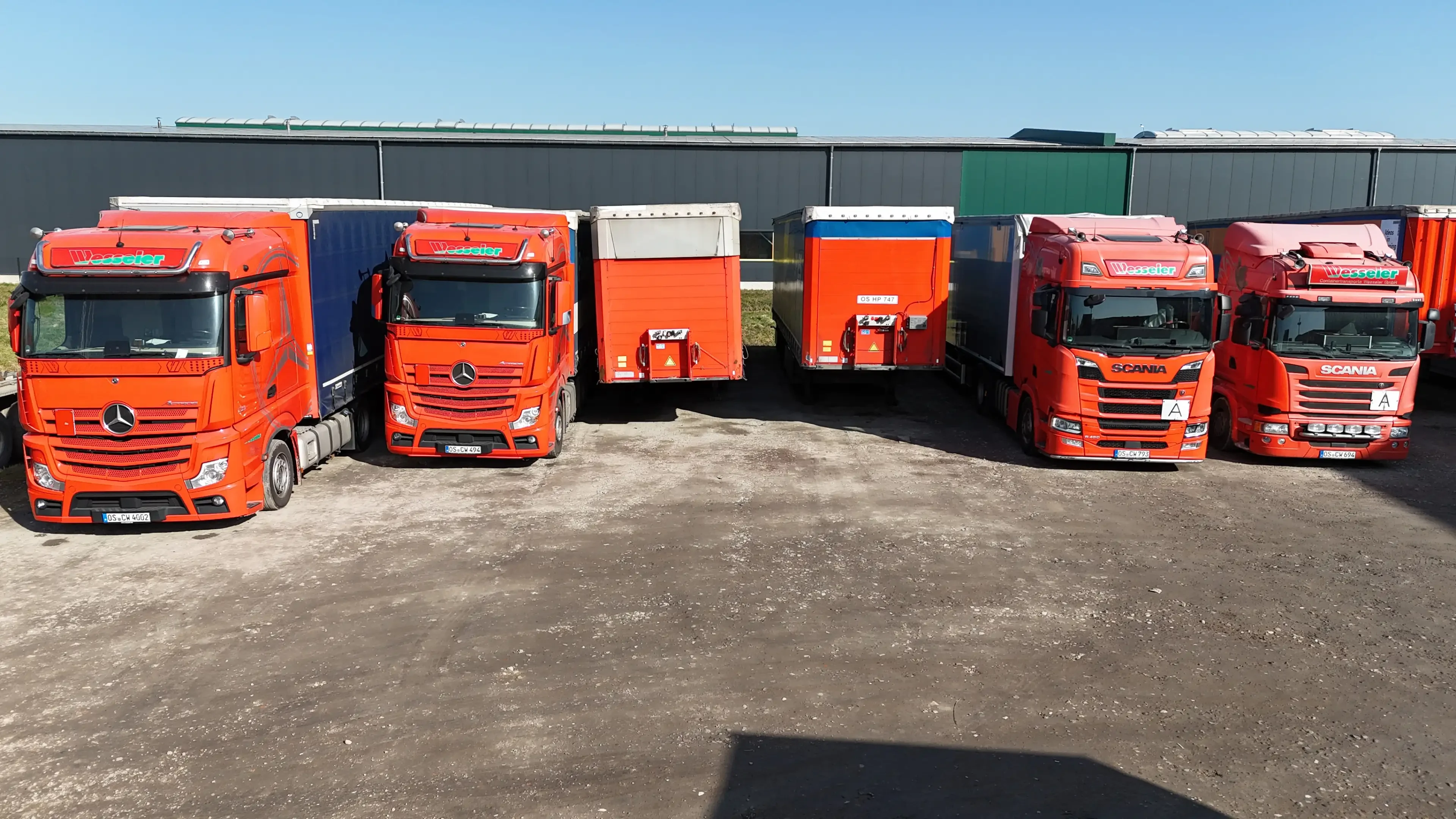 Mehrere rote LKWs und Anhänger auf einem Firmengelände bei sonnigem Wetter