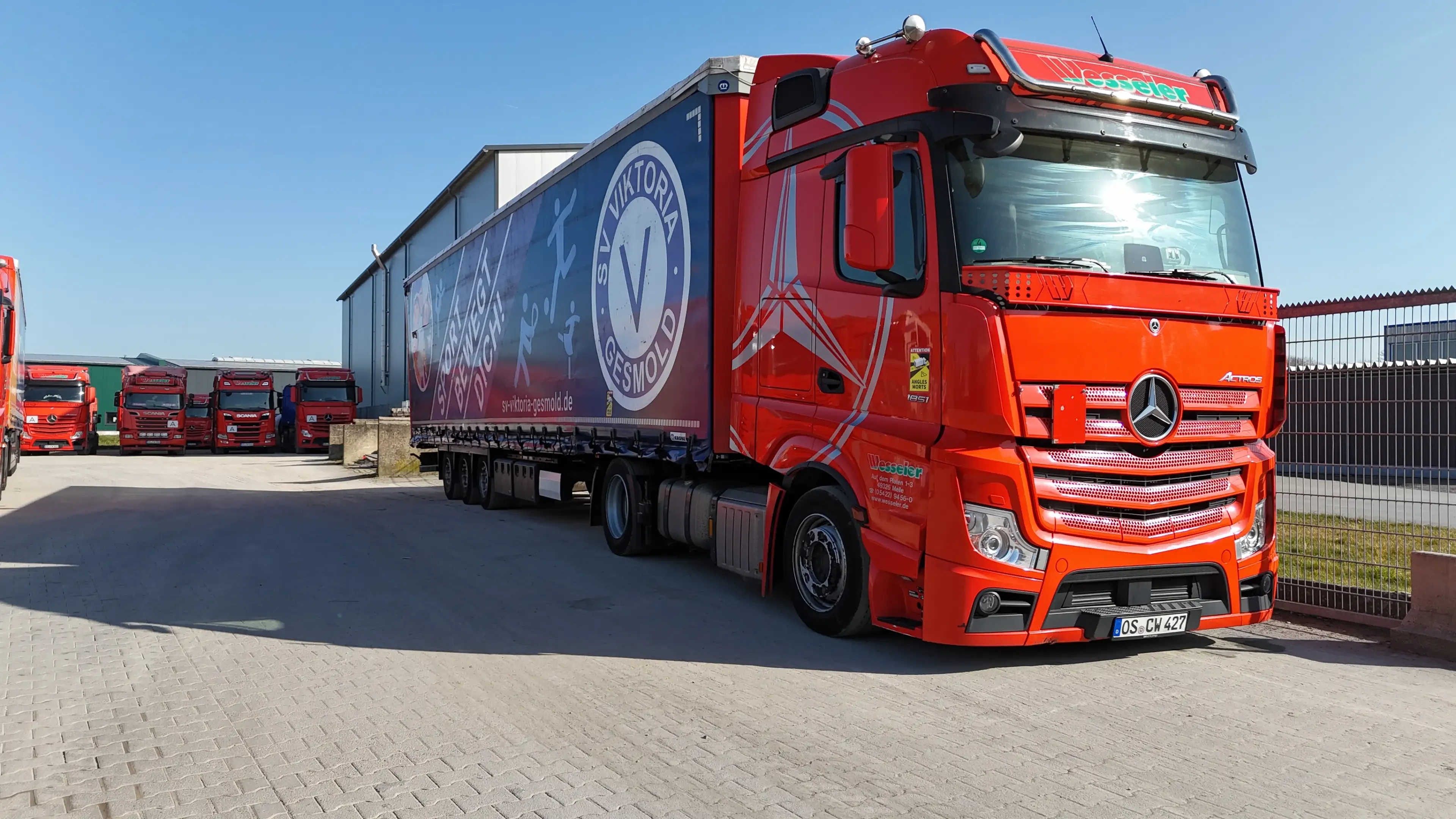 Roter LKW mit Werbung des SV Viktoria Gesmold auf dem Auflieger vor einer Halle