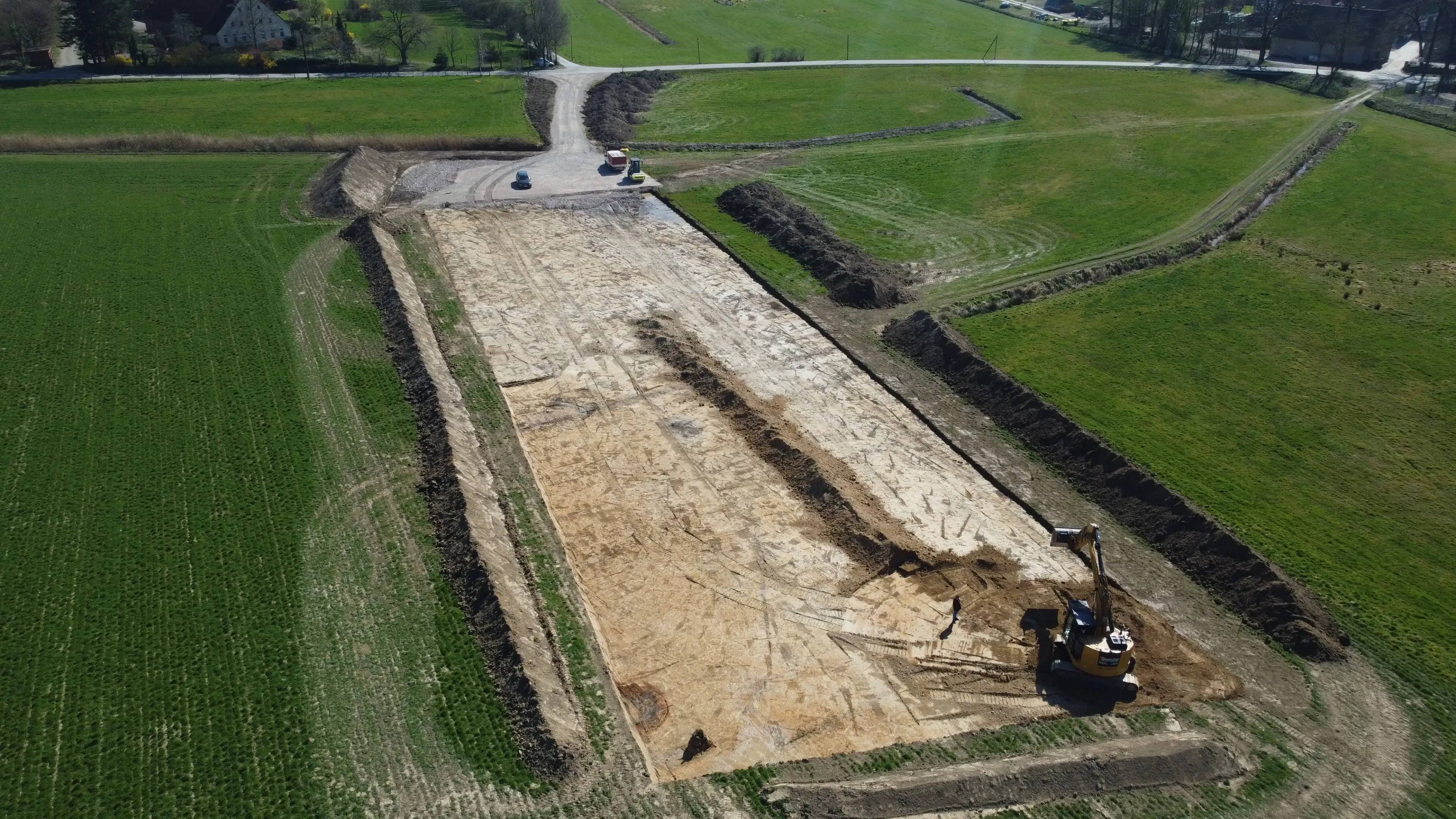 Bauarbeiten auf einem Feld mit Bagger und Fahrzeugen, Luftaufnahme einer Baustelle