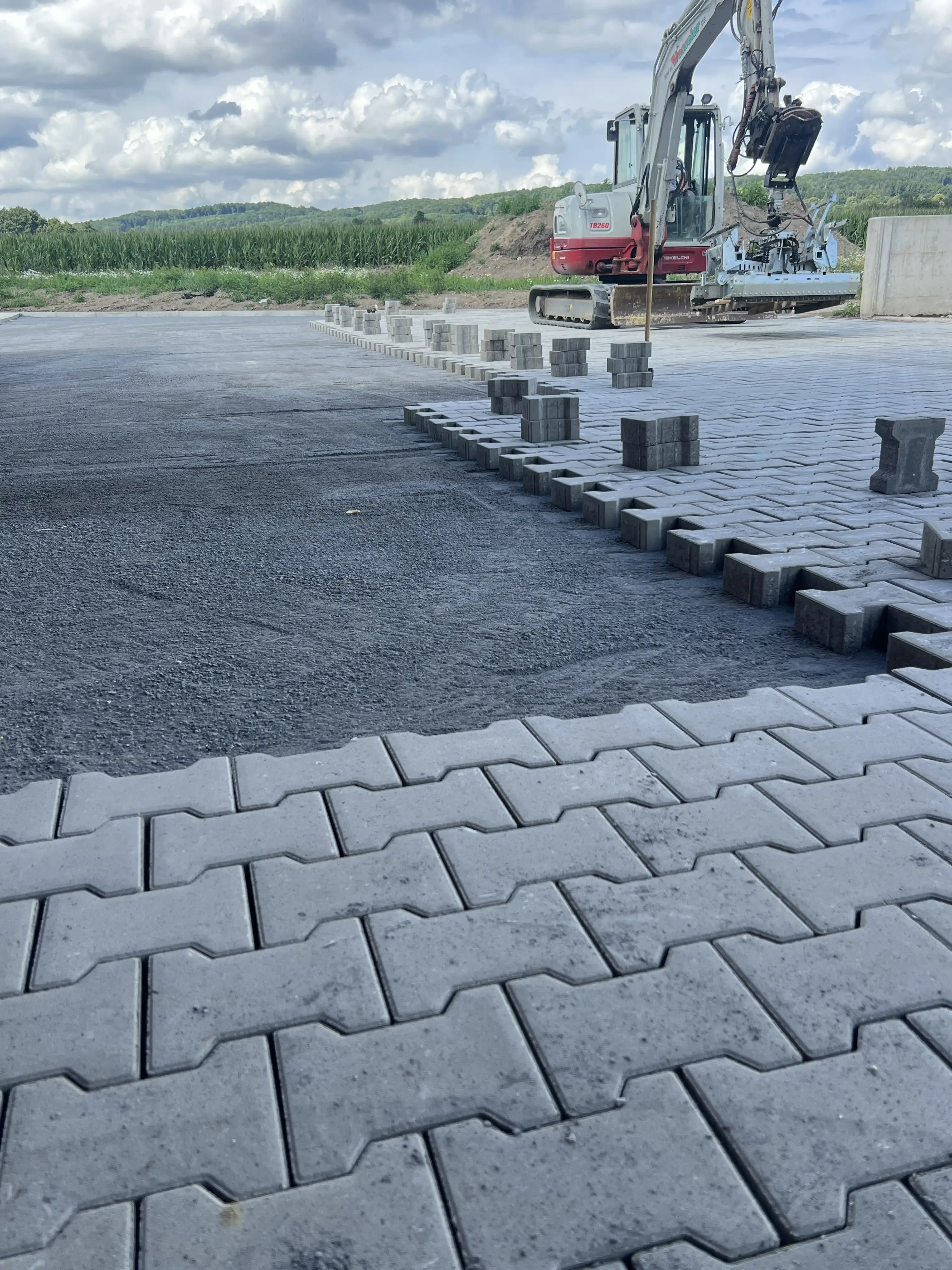 Verlegung von Betonpflastersteinen auf einer Baustelle mit Baumaschine im Hintergrund