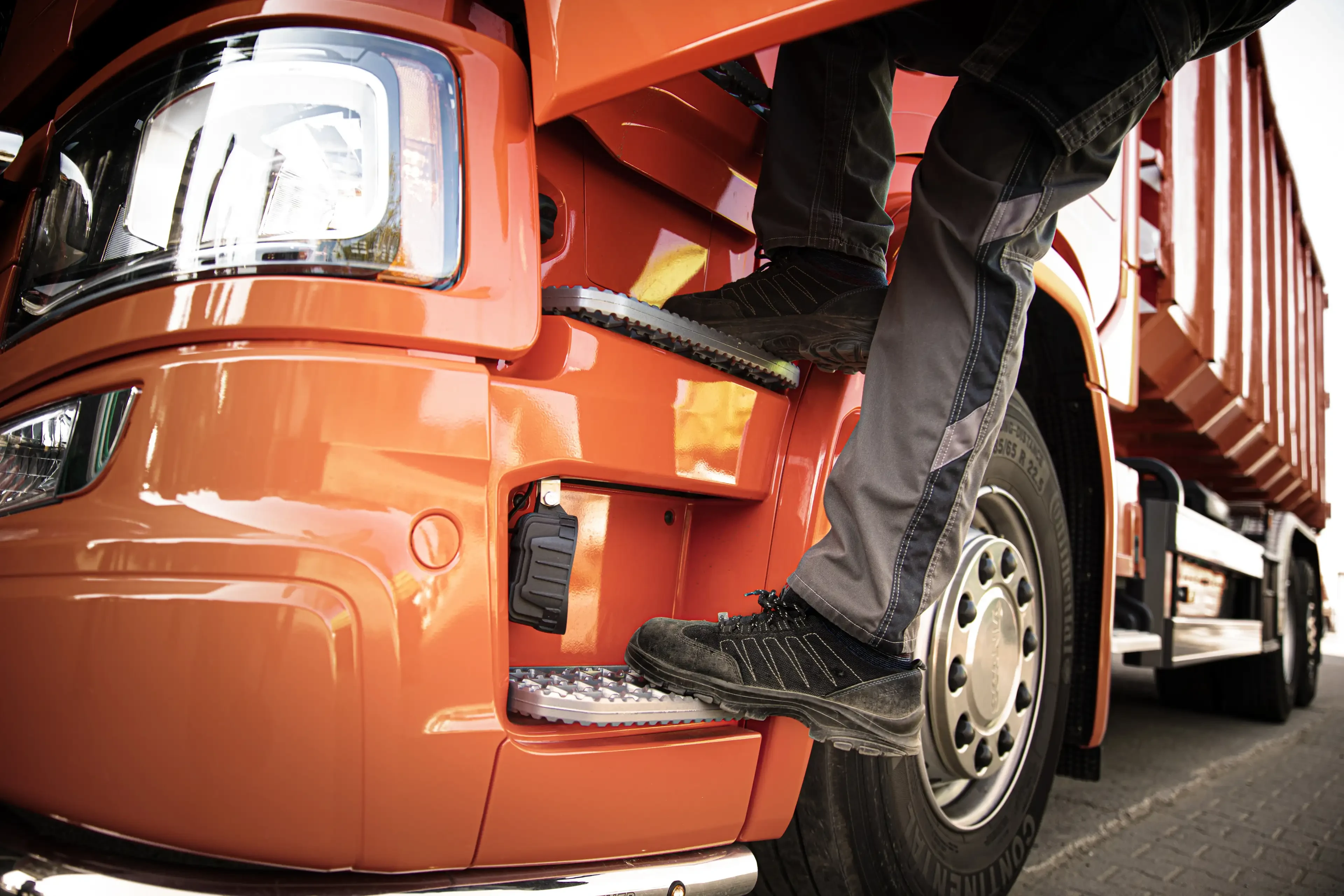 Person steigt auf die Trittstufen eines orangefarbenen Lkw-Fahrerhauses