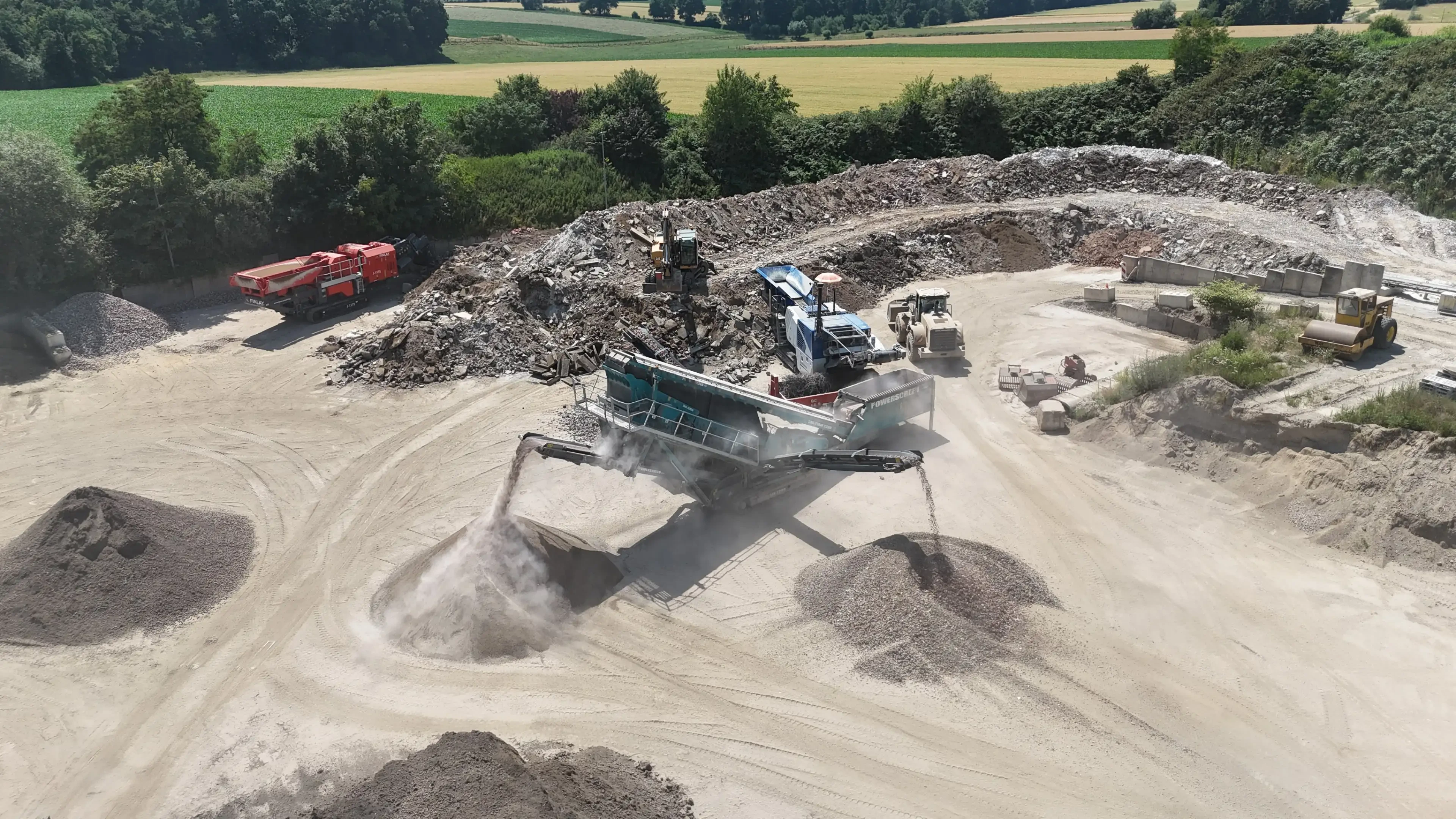 Baustelle mit Brechanlage und Bagger bei der Verarbeitung von Bauschutt im Freien