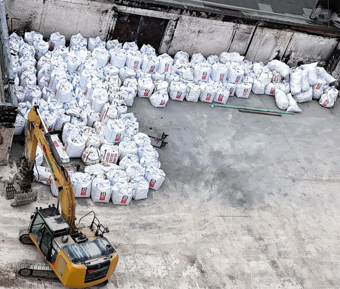 Baugelände mit Bagger und zahlreichen weißen Big Bags vor einer alten Mauer
