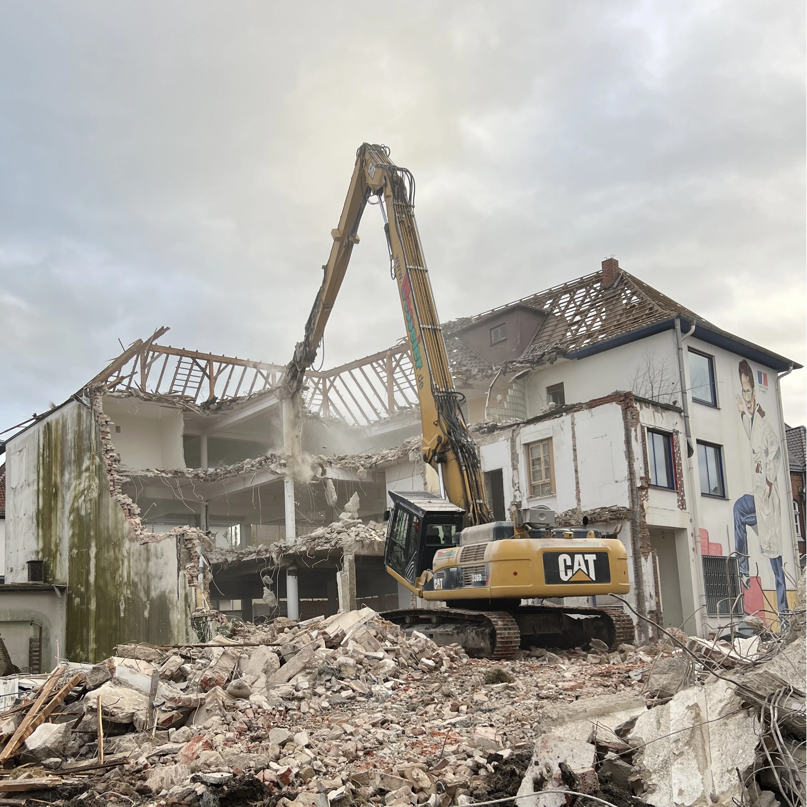 Abriss eines Gebudes mit CAT-Bagger, Baustelle mit Trfcmmern und teilweise zerstf6rtem Dachstuhl