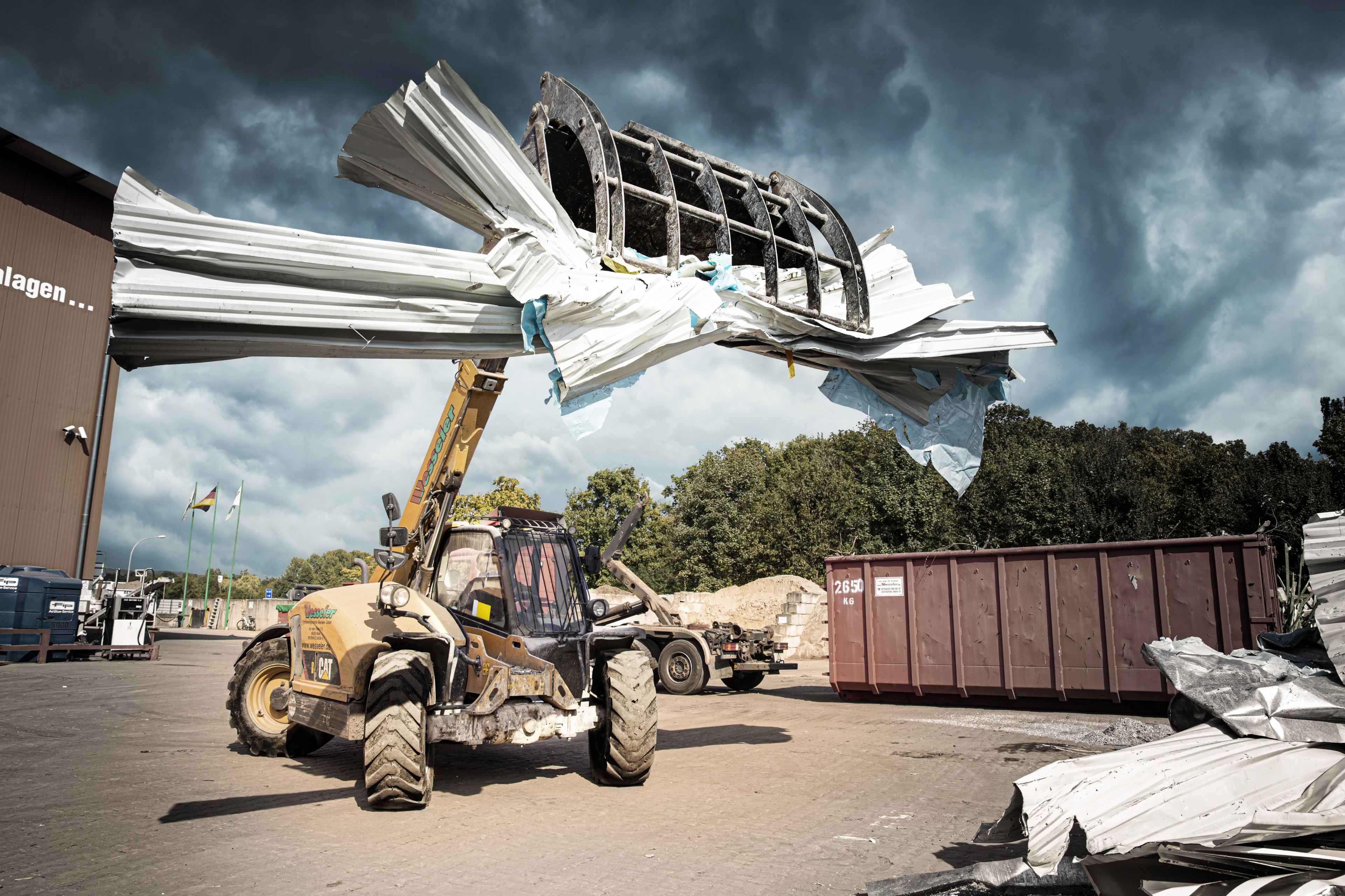 Teleskoplader hebt Altmetall auf einem Recyclinghof bei bewölktem Himmel