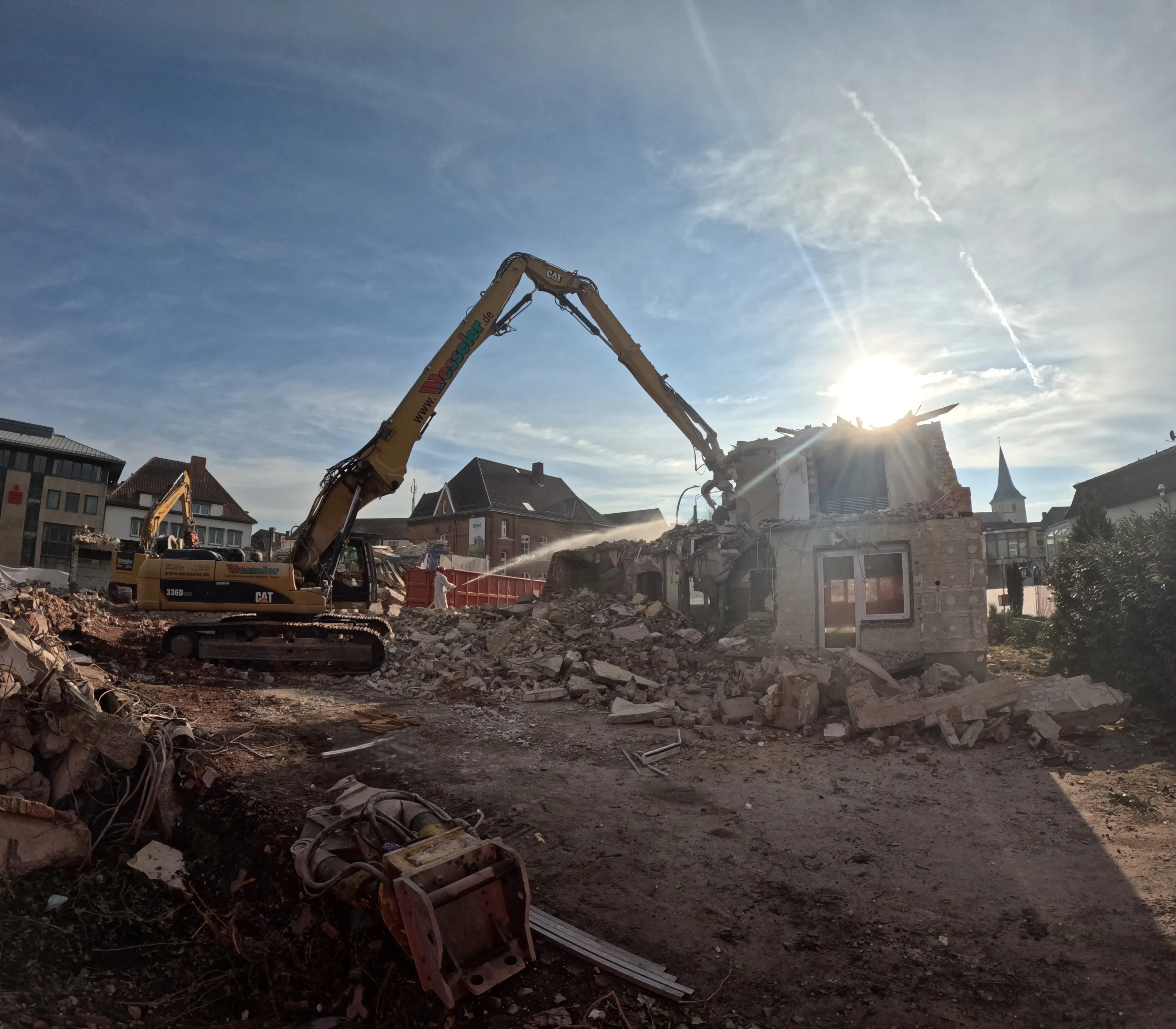 Bagger bei Abriss eines Hauses auf einer Baustelle mit Sonnenschein im Hintergrund