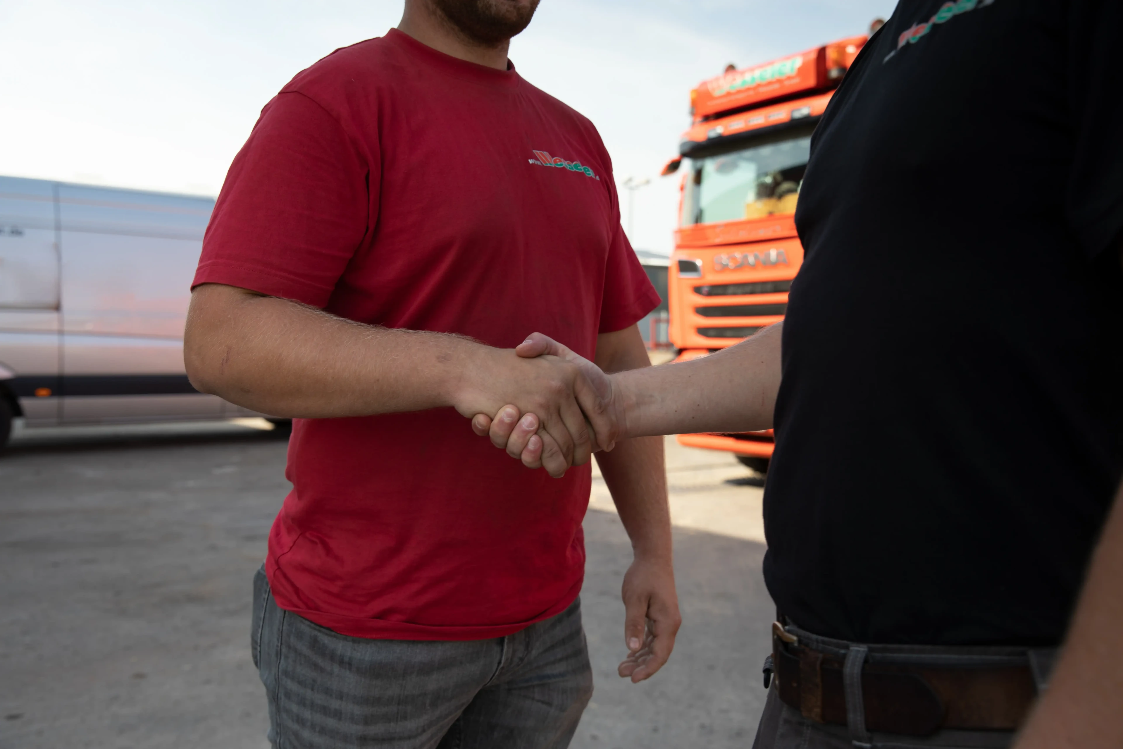 Zwei Männer geben sich die Hand vor einem LKW auf einem Firmengelände