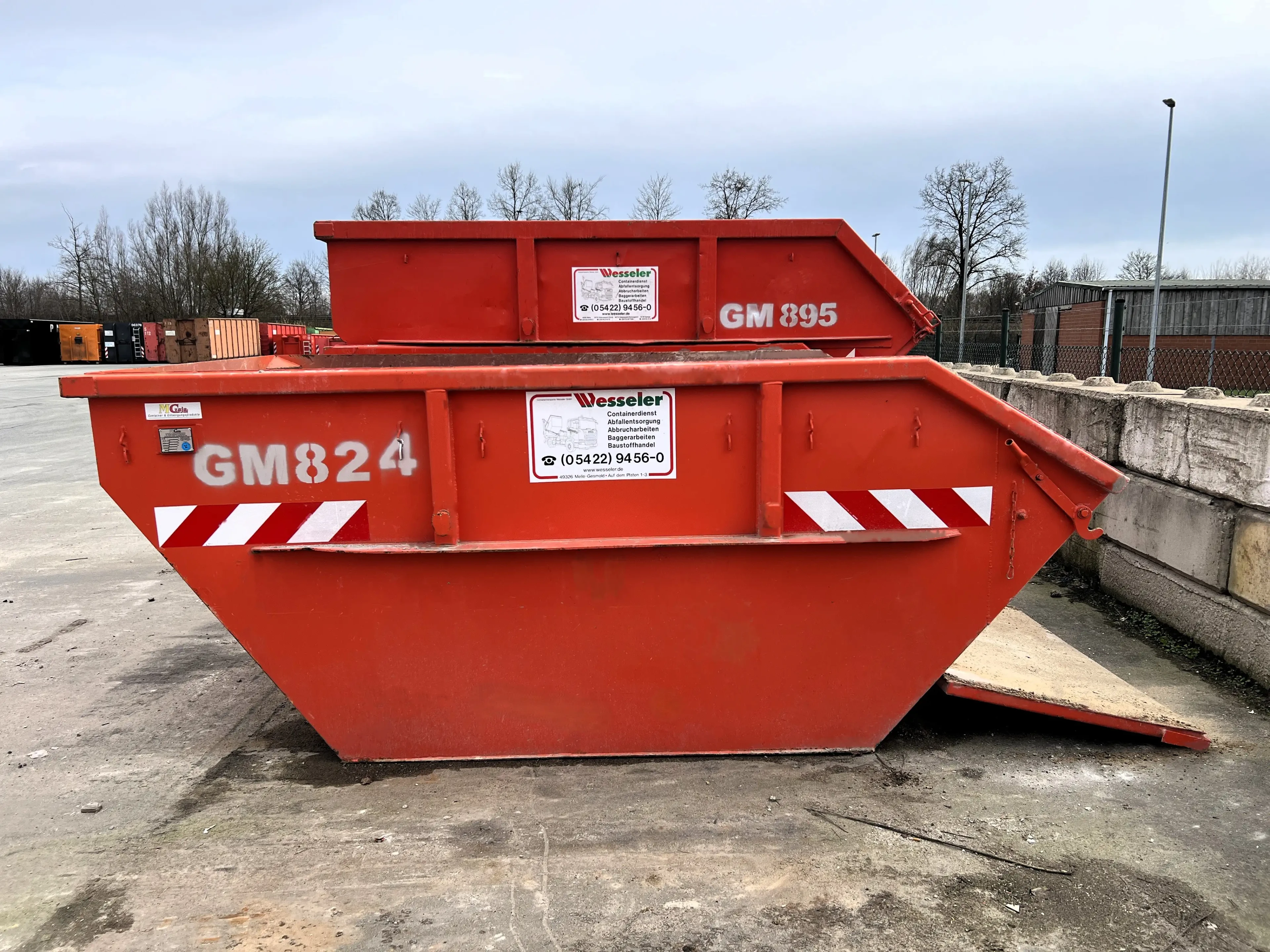 Zwei rote Abfallcontainer der Firma Wesseler mit den Nummern GM824 und GM895 auf einem Betriebshof.