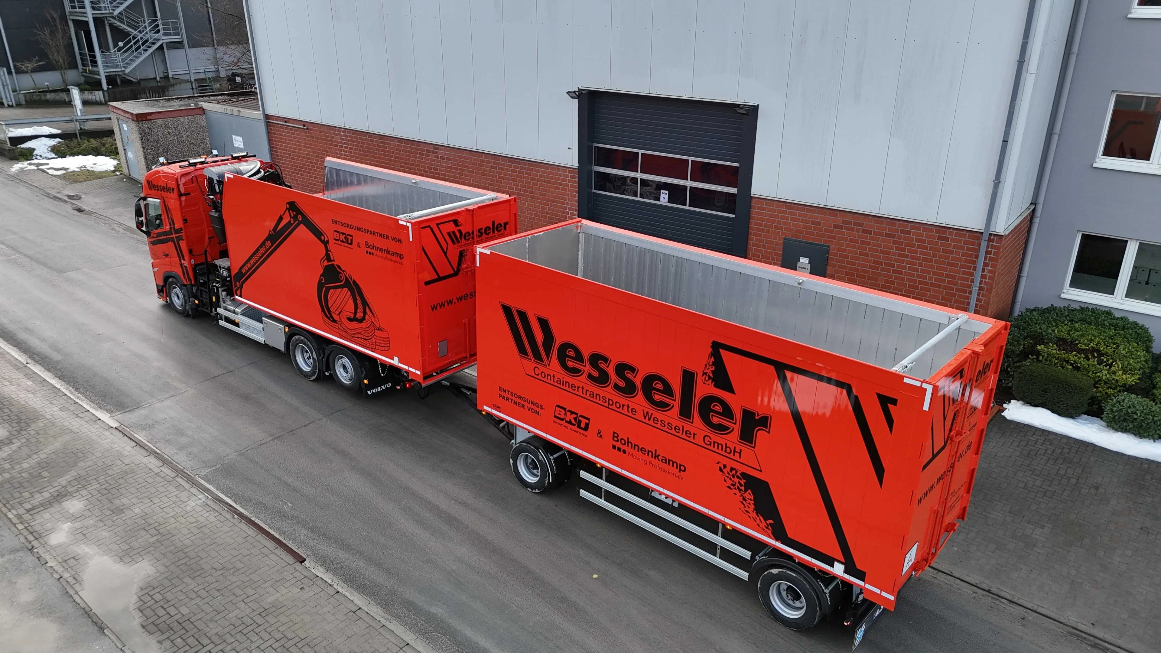 Zwei orange Containertransporter der Firma Wesseler vor einer Lagerhalle
