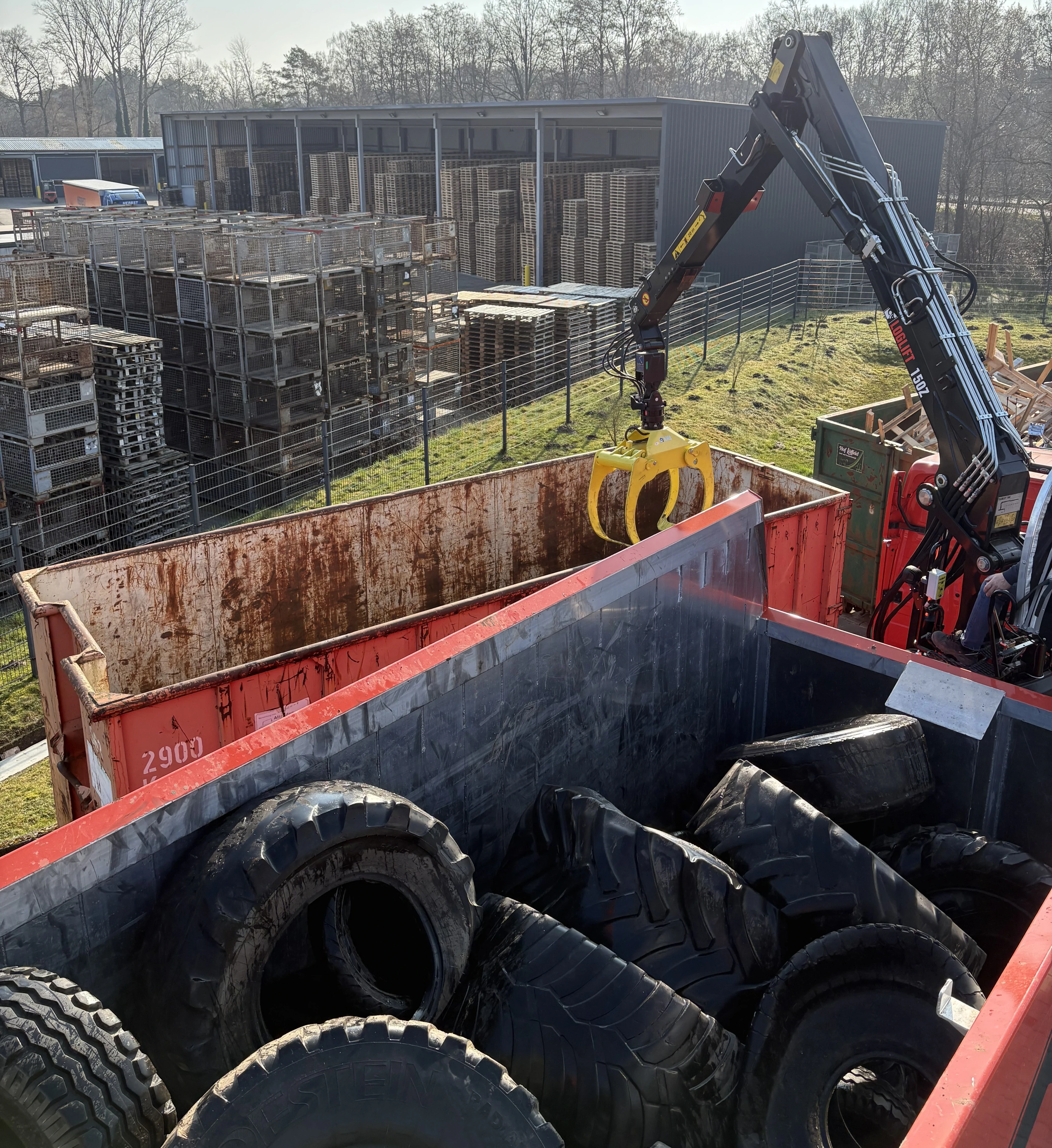 Reifenwagen mit Altreifen und Greifarm beim Recycling auf einem Industriegelände