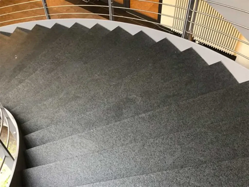 Moderne Treppenanlage mit grauem Steinbelag und Edelstahlgeländer in einem Innenraum