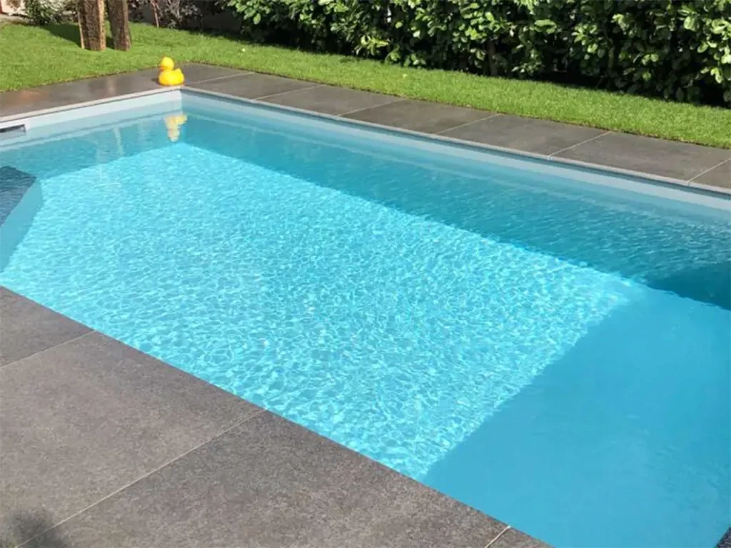 Moderne Poolumrandungen aus Steinplatten an einem Swimmingpool mit klar blauem Wasser