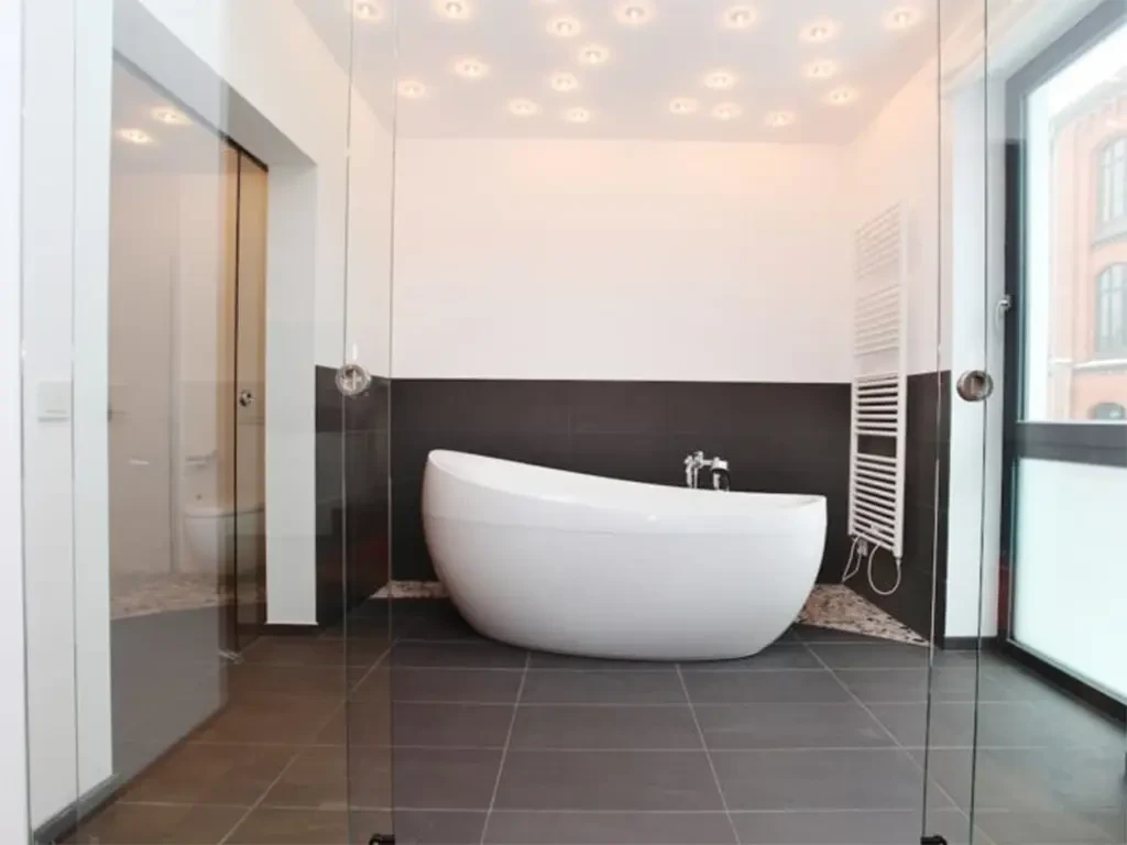 Moderne freistehende Badewanne in elegantem Badezimmer mit dunklen Fliesen und stilvoller Beleuchtung