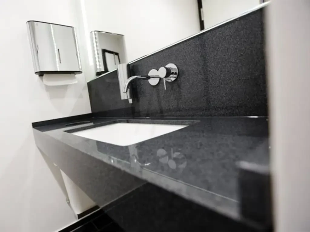 Moderner Waschtisch mit schwarzer Steinplatte und Wandarmatur in einem Badezimmer