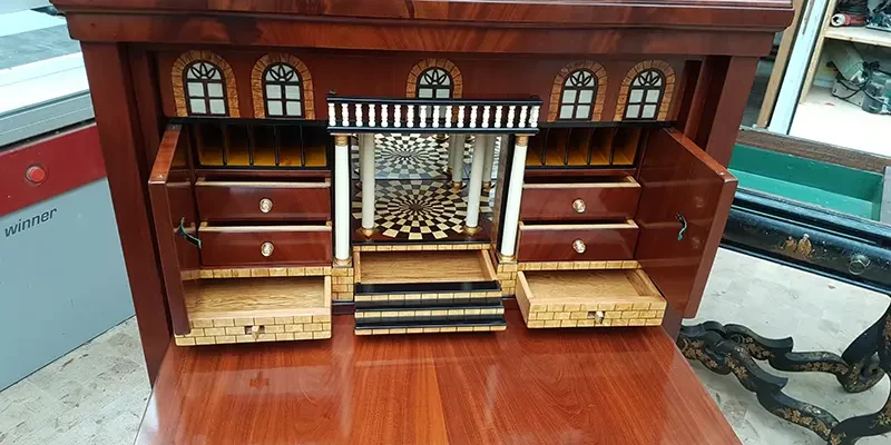 Detailansicht eines kunstvoll gearbeiteten Schreibtisches mit Schubladen, Intarsien und architektonischen Elementen im klassischen Stil