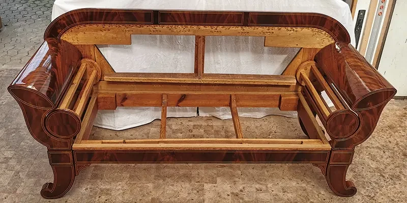 Holzgestell eines antiken Sofas ohne Polsterung, sichtbar restauriert