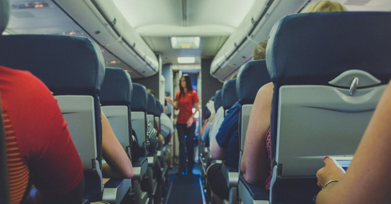 Flugzeugsitze in einer Passagierkabine mit Flugbegleiterin im Gang