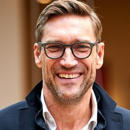 Udo Barth, Porträt eines Mannes mit braunen Haaren und Bart, trägt einen dunklen Mantel und weißes Hemd