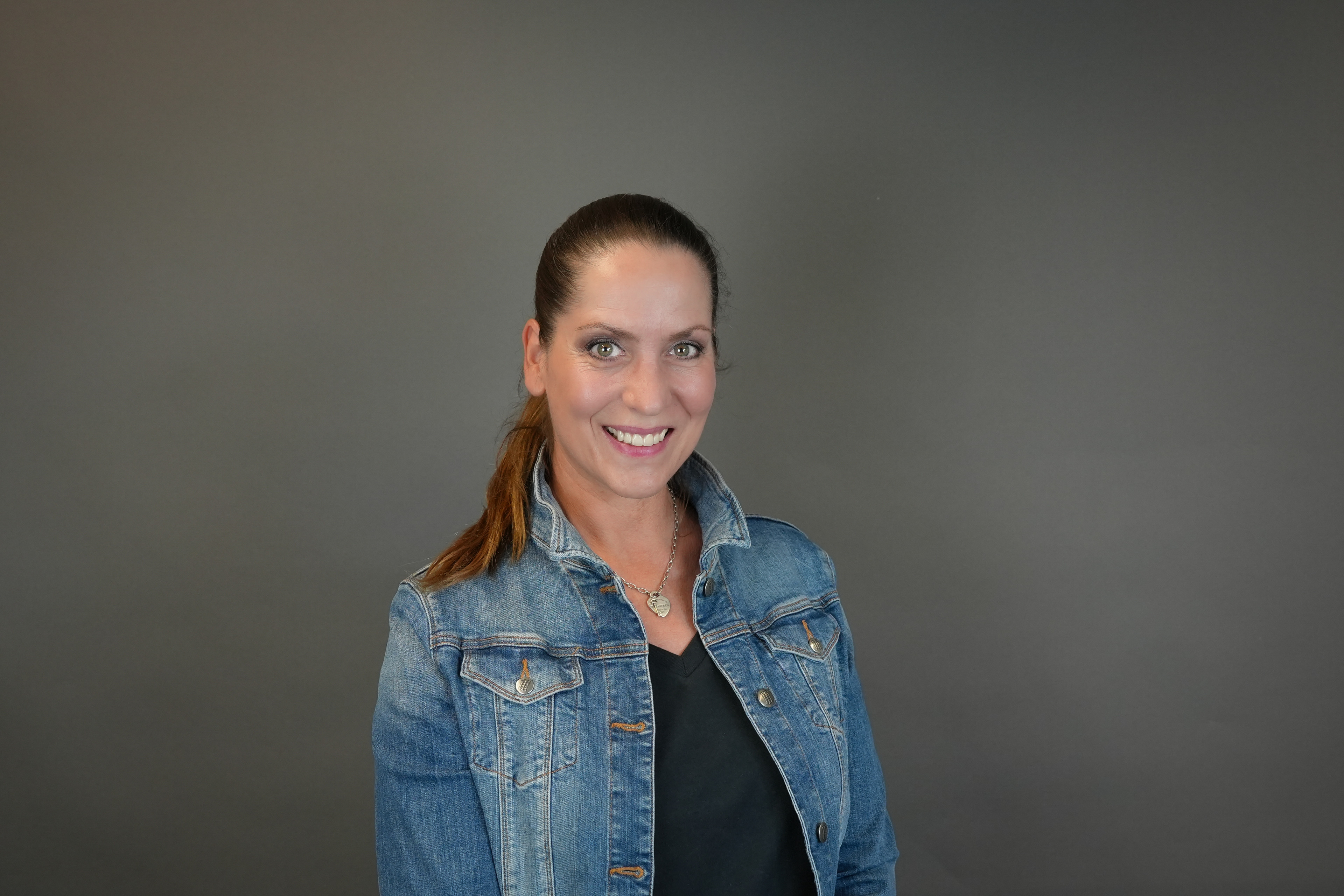 Anna Dau als Sales Managerin im Portrait mit Jeansjacke vor grauem Hintergrund