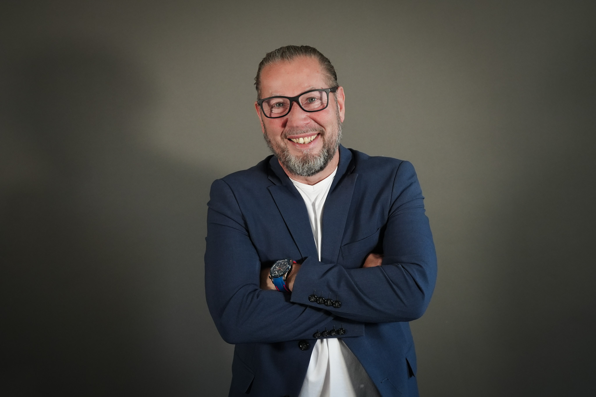 Kai Burkhardt im blauen Sakko mit verschränkten Armen vor neutralem Hintergrund