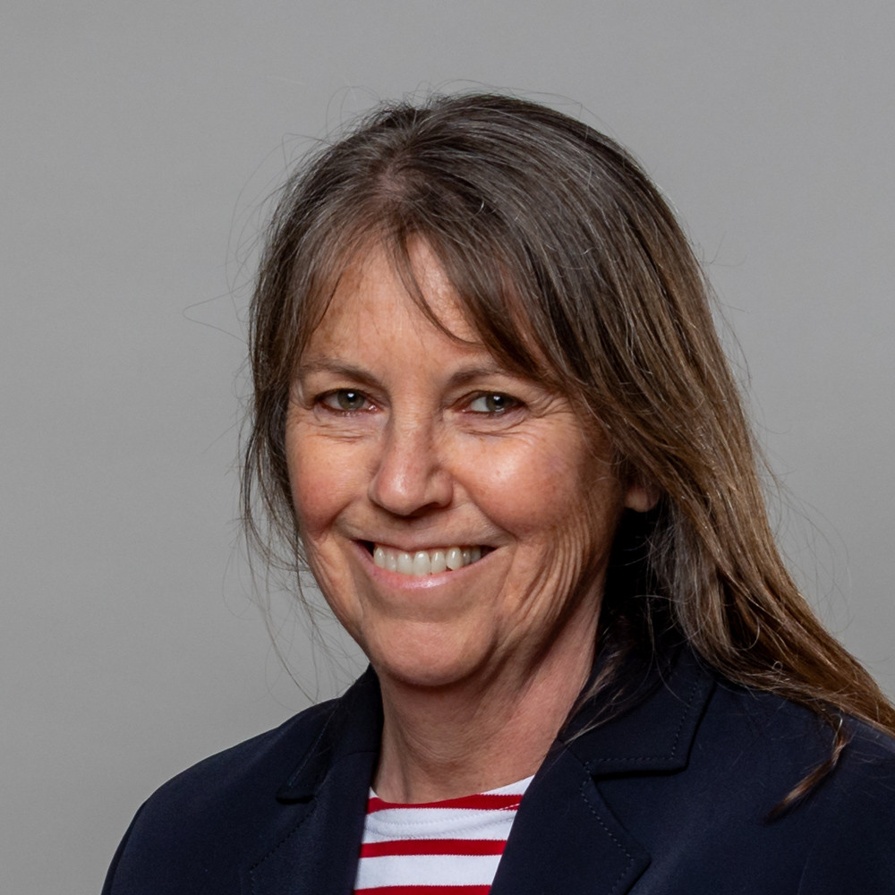 Porträt von Birgit Schaper-Dworschak Birgit Schaper-Dworschak im Porträt mit dunklem Blazer und gestreiftem Shirt vor grauem Hintergrund