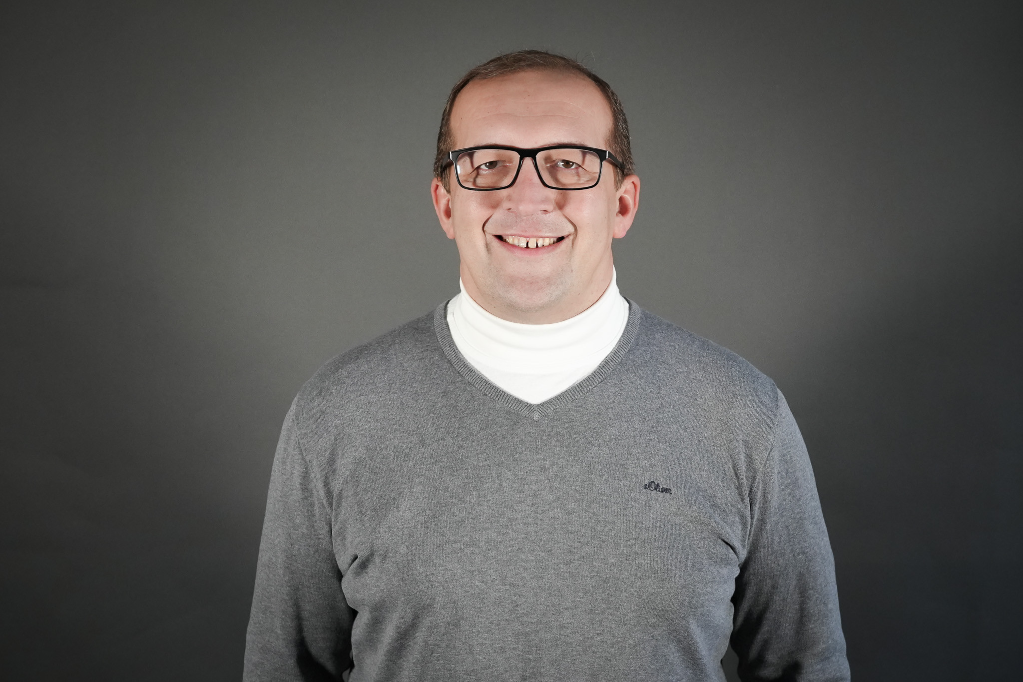 Hartmut Wolf im grauen Pullover vor neutralem Hintergrund