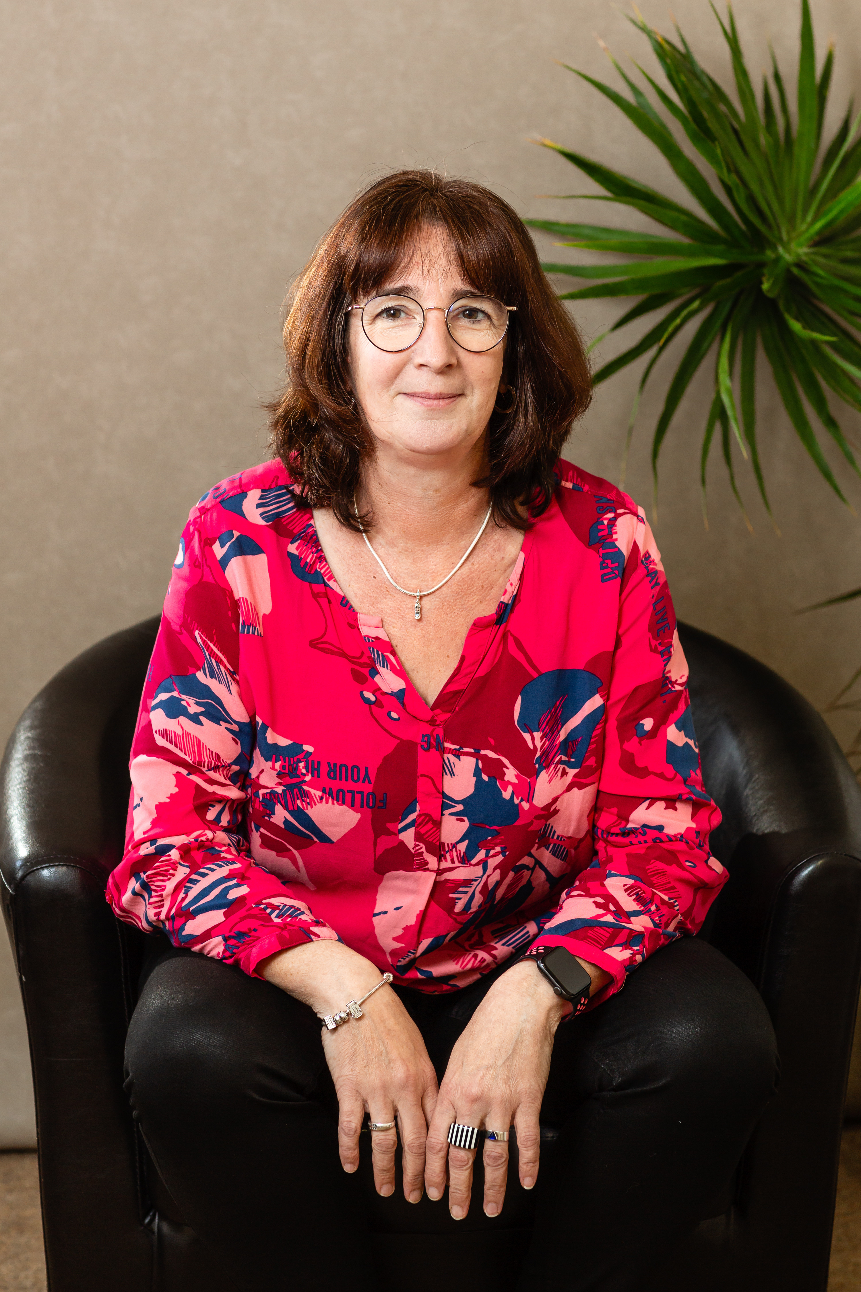 Businessfoto 2023 von Jana auf einem schwarzen Ledersessel mit auffälliger roter Bluse