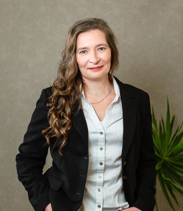 Frau im Business-Outfit mit weißer Bluse und schwarzem Blazer vor neutralem Hintergrund