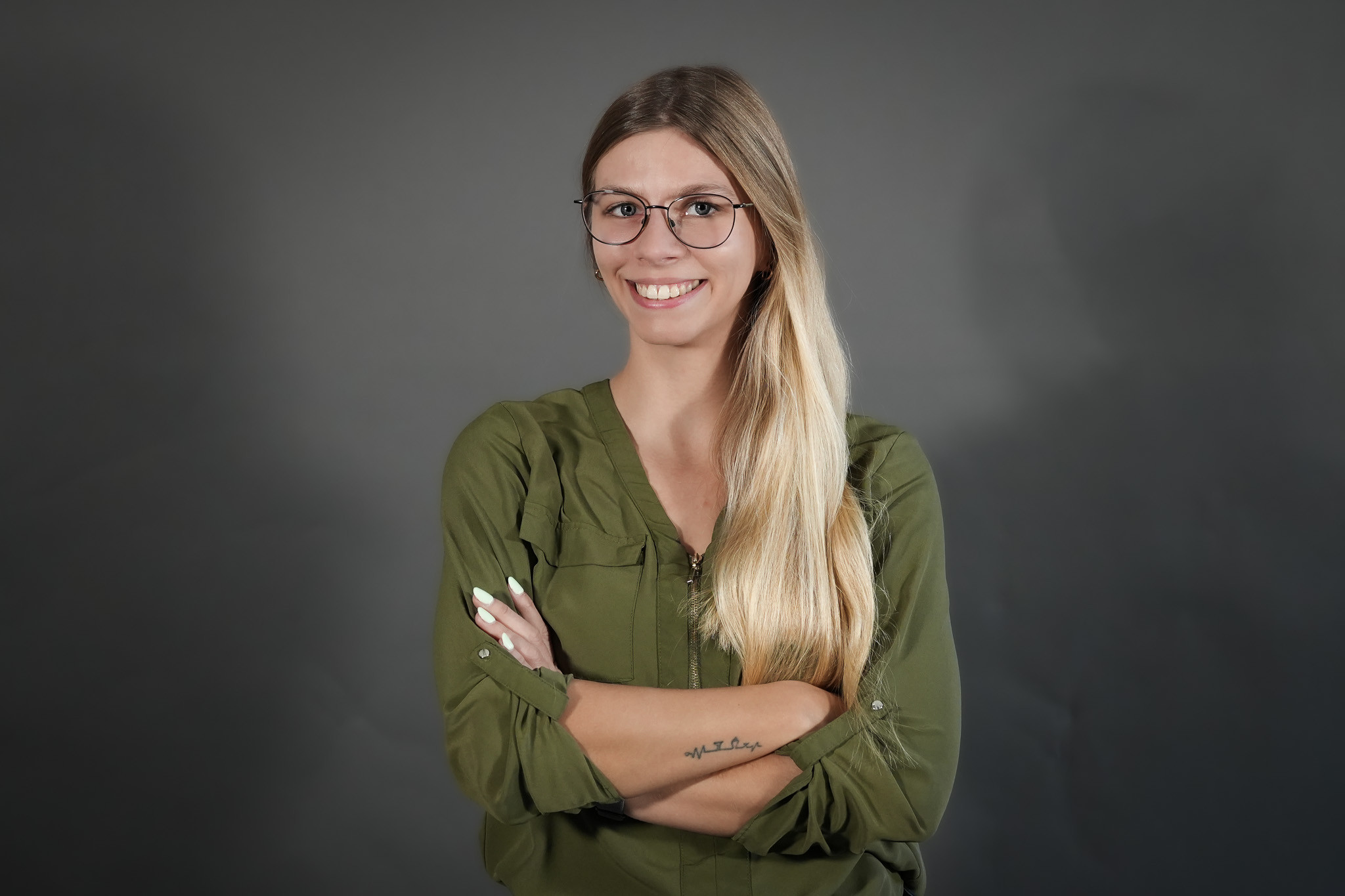 Frau mit langen blonden Haaren und grünem Hemd vor grauem Hintergrund