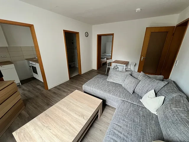 Apartment – modernes kleines Apartment mit Wohnzimmer, Küche und Schlafzimmer Modern eingerichtetes kleines Apartment mit Wohnzimmer, grauem Sofa und Blick auf Küche und Schlafzimmer