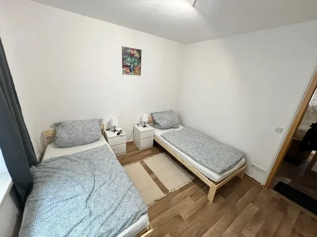 Apartment – Schlafzimmer mit zwei Einzelbetten und moderner Einrichtung Apartment – modernes Schlafzimmer mit zwei Einzelbetten, Nachttischen und Holzboden